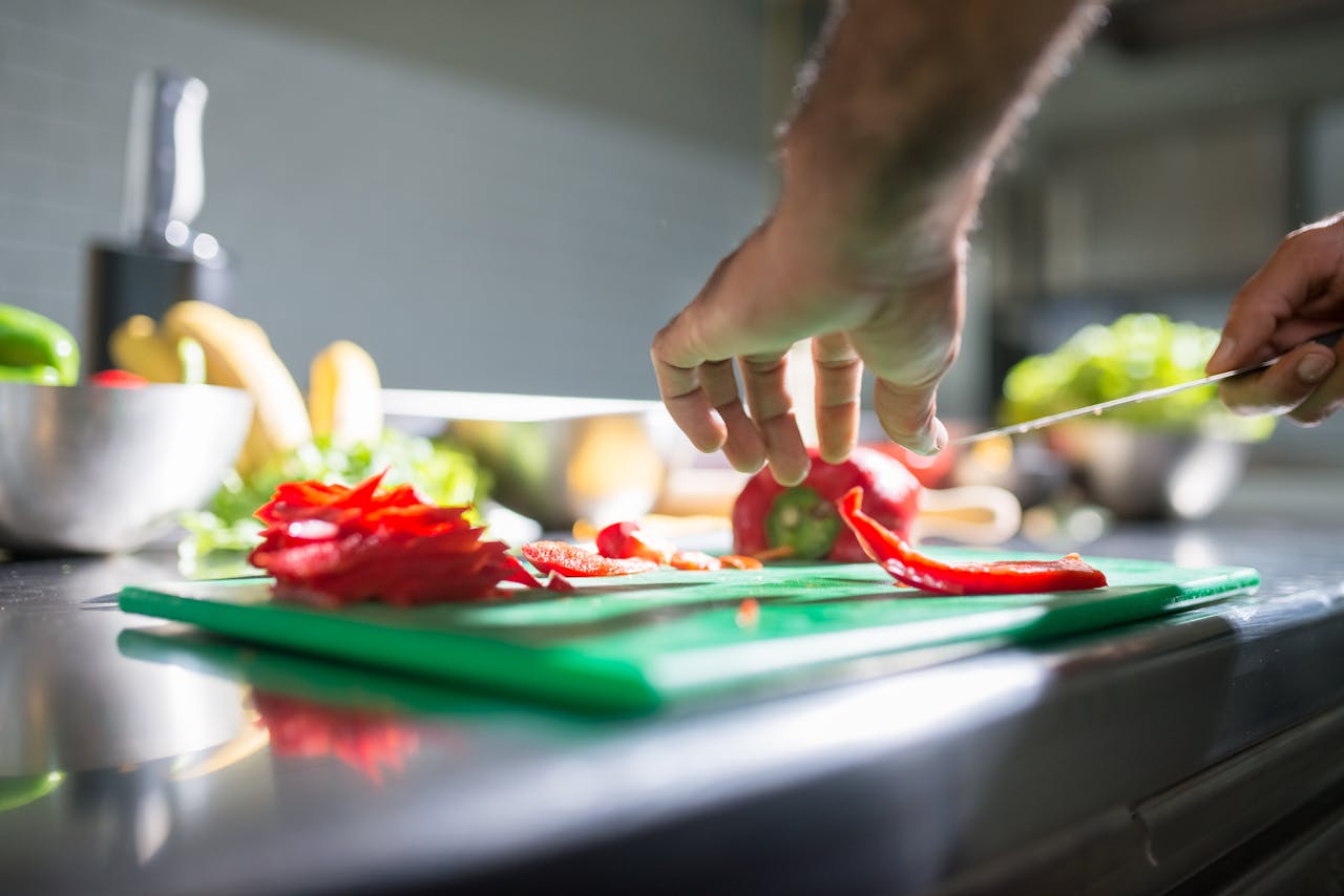 services-01 Hands slicing red bell pepper on a chopping board in a kitchen setting, ideal for culinary visuals.