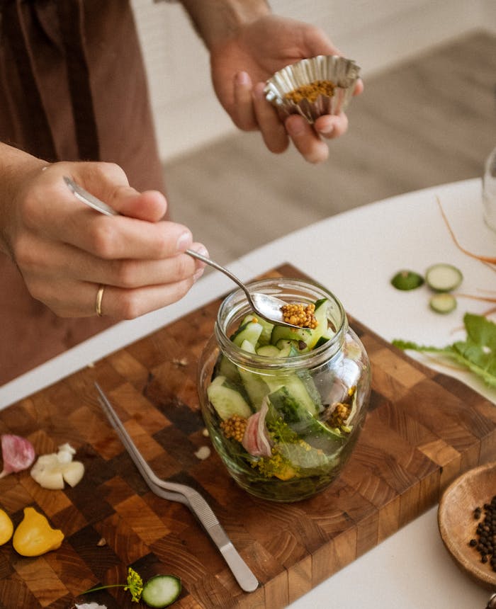 who-we-are Hands carefully preparing pickled vegetables with cucumbers and garlic in a kitchen setting.